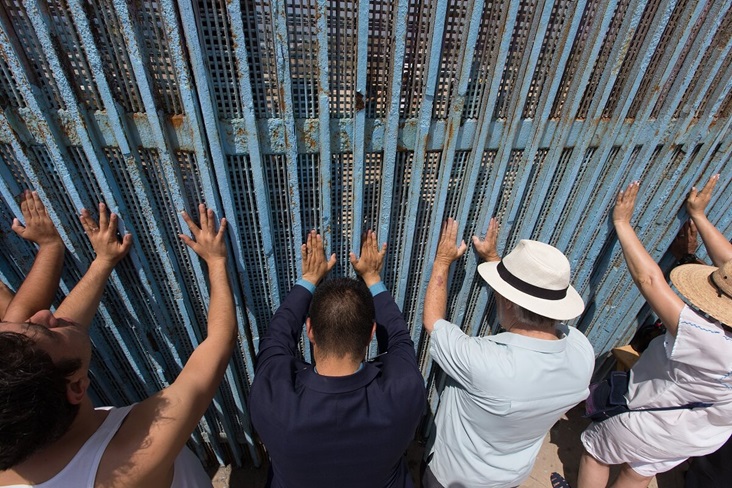 The Revs. Joel Hortiales (center, in blue blazer) and David Farley (to Hortiales' right) join parishioners of the Border Church in Tijuana, Mexico, as they lift their arms skyward beneath the fence that marks the border with the U.S. Photo by Mike DuBose, UMNS.